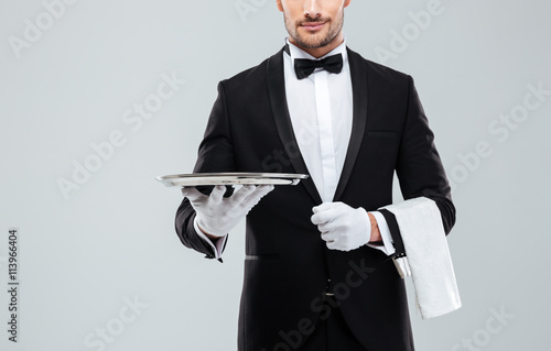 Waiter in tuxedo holding metal empty tray and napkin photo
