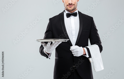 Fotografie Waiter in tuxedo holding metal empty tray and napkin
