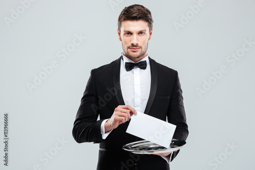 Handsome young waiter in tuxedo holding tray with blank card