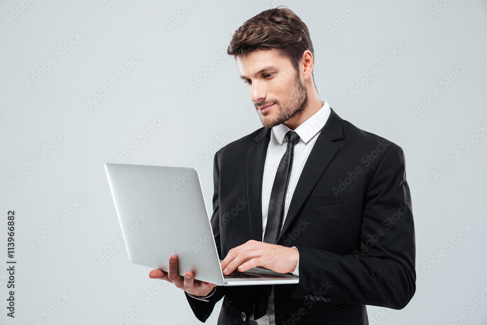 Handsome young businessman standing and using laptop Handsome young businessman standing and using laptop