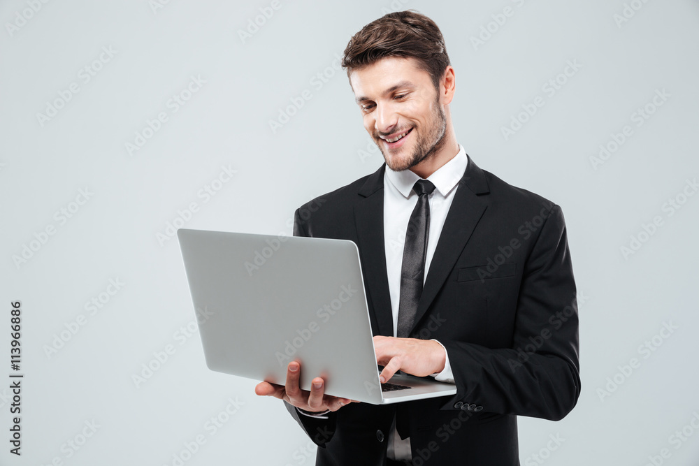 Cheerful young businessman smiling and using laptop Cheerful young businessman smiling and using laptop
