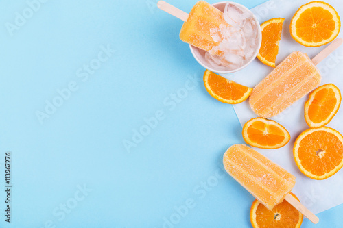 Homemade orange popsicles with orange slices on a paper and blue background. Top view with copyspace