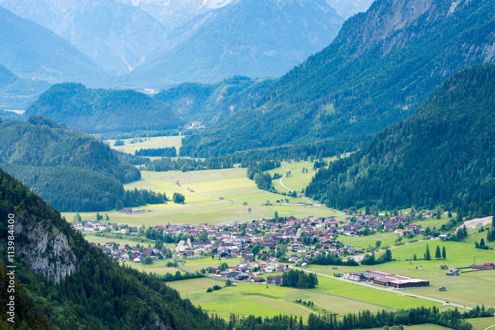 The village is in an alpine valley. Green fields in the mountains