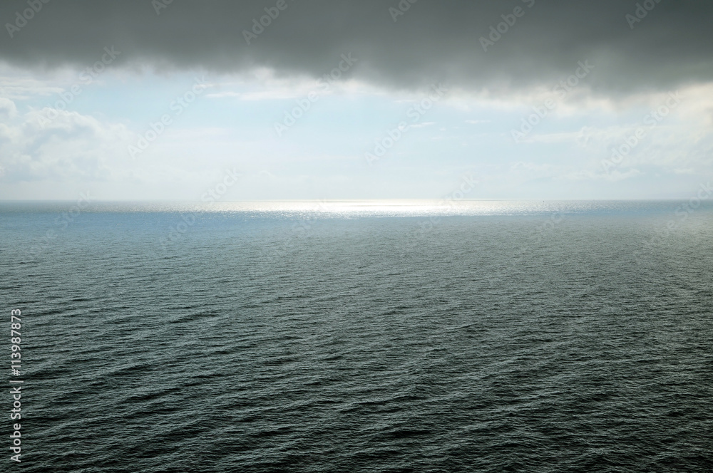 Fototapeta premium Black sea during a storm. A cloud hangs over water with waves, sunlight away.