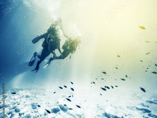Three scuba divers. Swimming with fishes. Vintage effect.