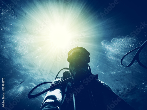 Man diving in the ocean with sun rays in the background.