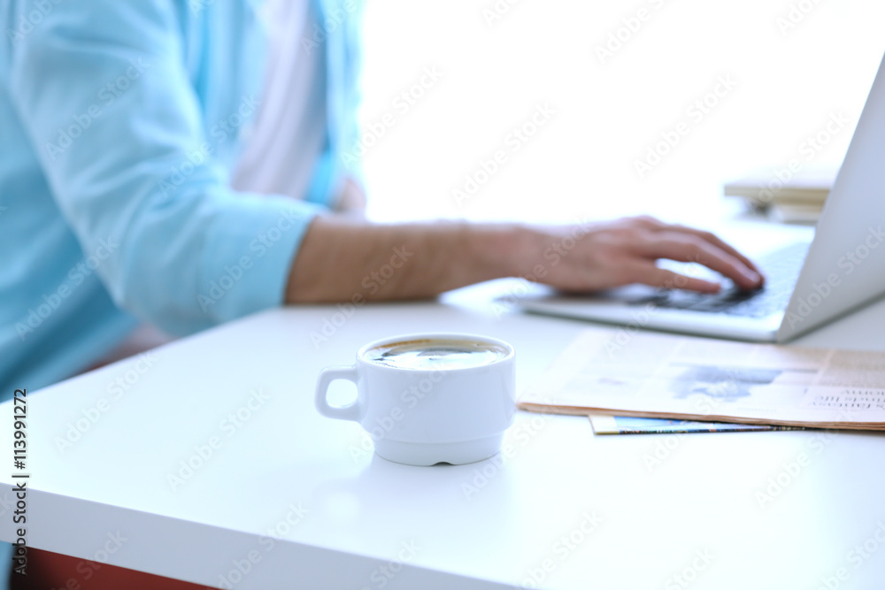 White cup of coffee and man working on background White cup of coffee and man working on background