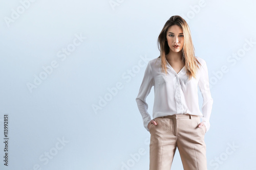 Beautiful young woman in a white shirt and beige pants on blue wall background © Africa Studio