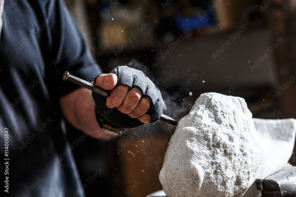 Close up of senior sculptor hands working on his marble sculpture in his workshop with hammer and chisel - obrazy, fototapety, plakaty 