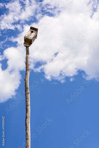 Old wooden birdhouse on a wooden post on the background of beautiful blue sky and clouds