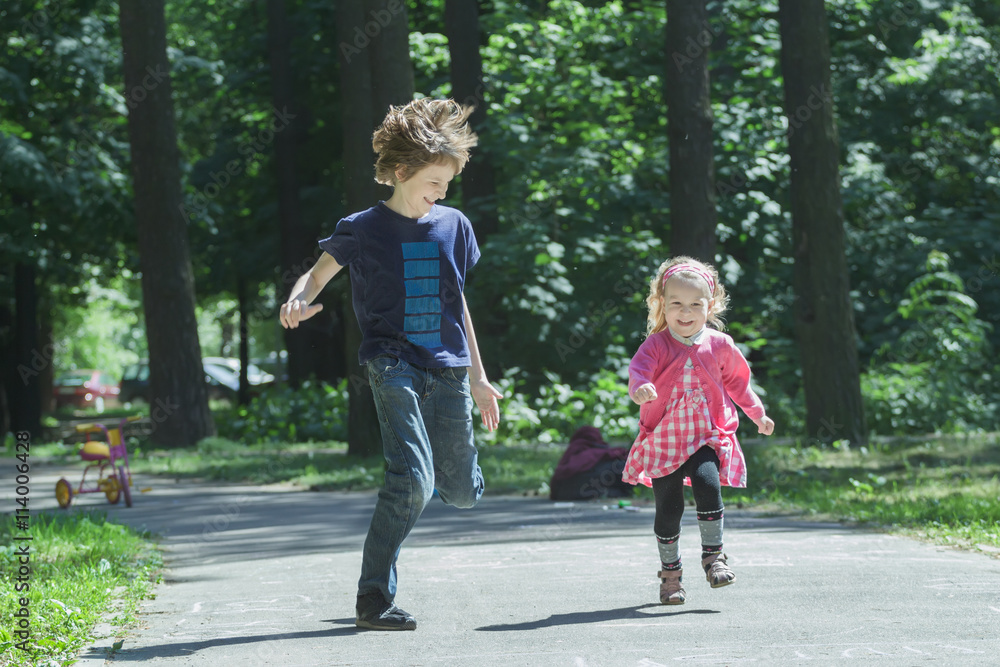 Naklejka premium Laughing sibling children playing tag and running on park asphalt footpath