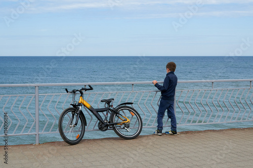 Мальчик с велосипедом смотрит на море стоя на набережной промеданте