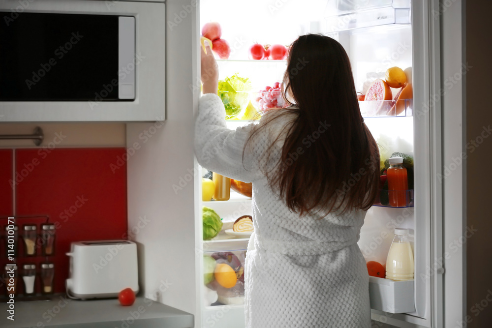 Young beautiful woman looking into fridge at night Young beautiful woman looking into fridge at night