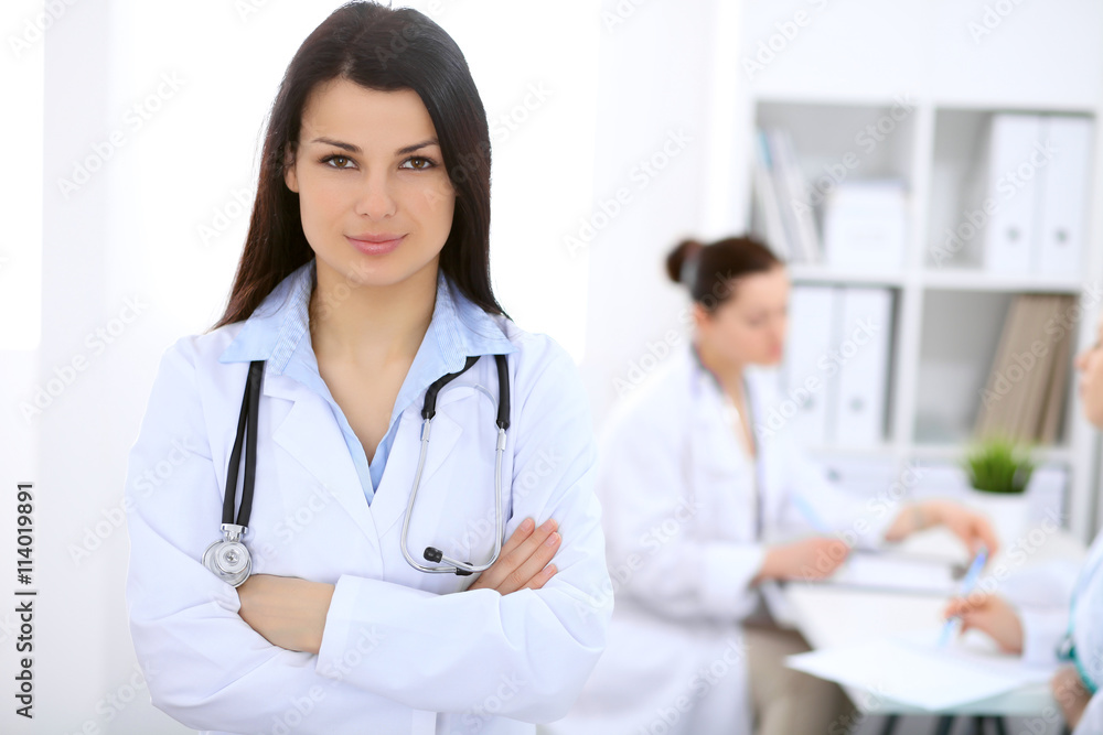 Brunette female doctor on the background of colleagues talking to each other in hospital Brunette female doctor on the background of colleagues talking to each other in hospital