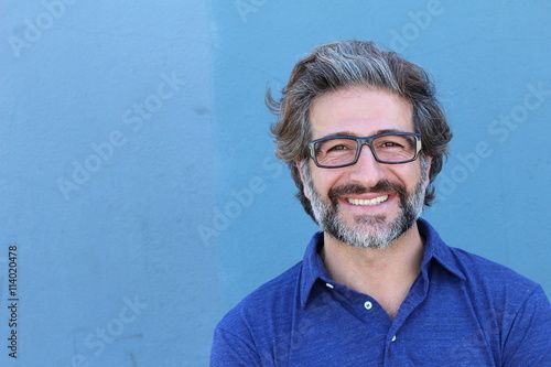 Portrait of stylish businessman with glasses smiling on blue wall background with copy space