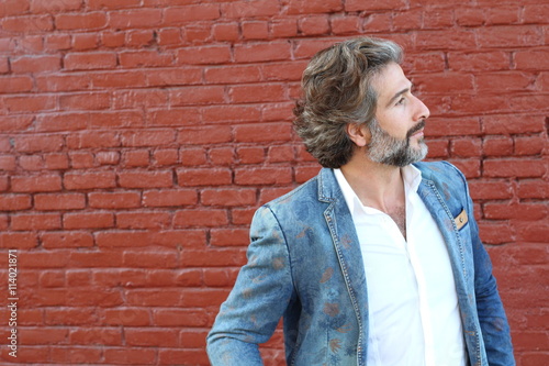 Thoughtful senior male teacher or businessman standing thinking in front of a red brick wall with copyspace, head and shoulders profile view