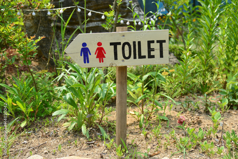 Wooden sign pointing way in garden to restrooms or toilets