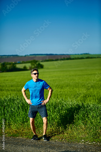 man runner athlete jogging along a green field in the early morning. man fitness sunset jogging workout wellness concept. free space in front of the person