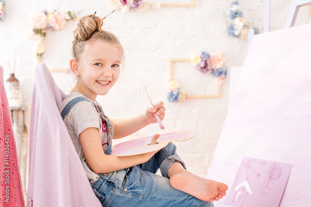 Little artist in denim overalls painting brushes on the easel in her studio Little artist in denim overalls painting brushes on the easel in her studio