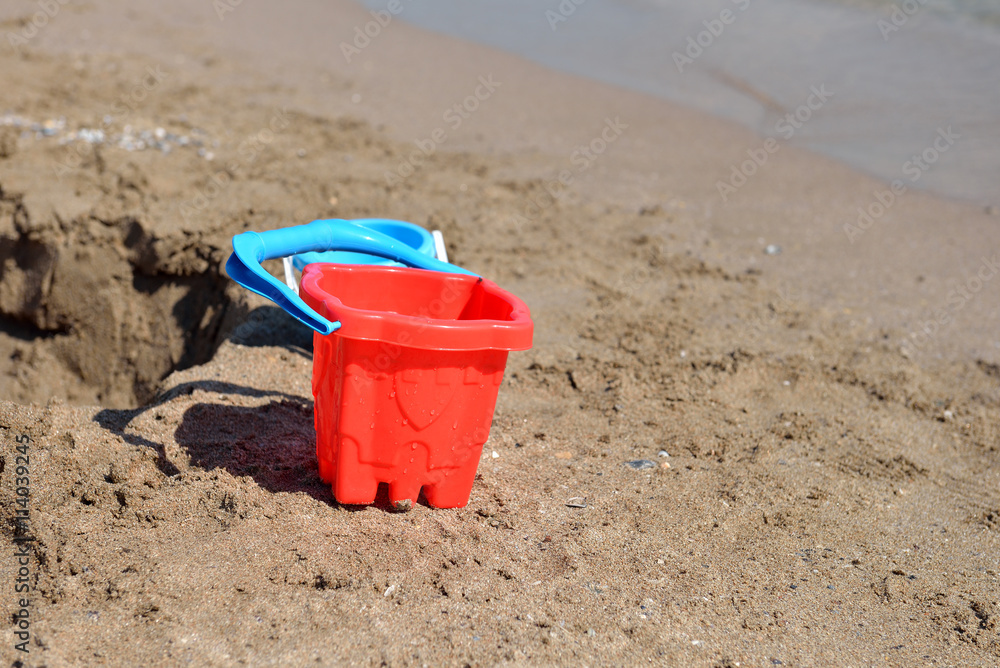 Red bucket on the wet sand on the beach in a summer sunny day. C Red bucket on the wet sand on the beach in a summer sunny day. C