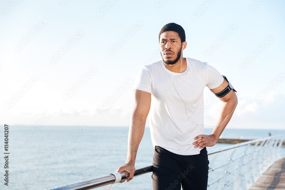 Sportsman listening to music using earphones standing on pier