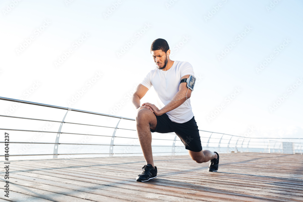 Obraz premium Sportsman warming up and stretching legs on pier