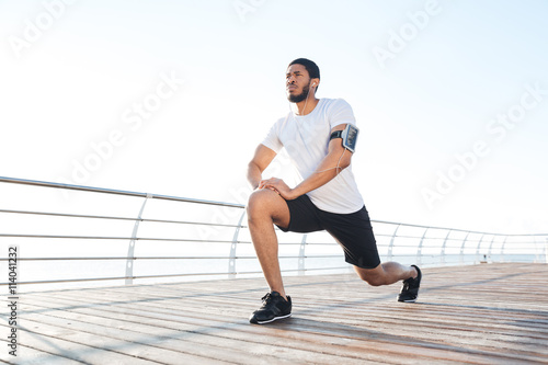Sportsman stretching legs and listening to music from smartphone