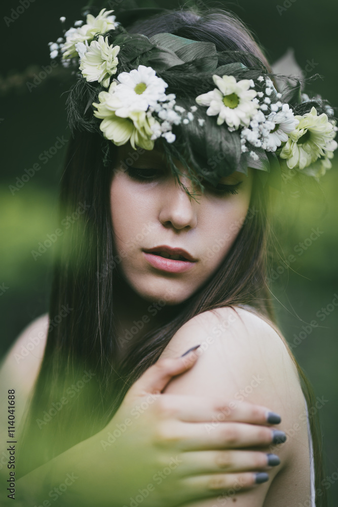 Naklejka premium Outdoor portrait of beautiful young woman in a white dress wearing floral wreath.