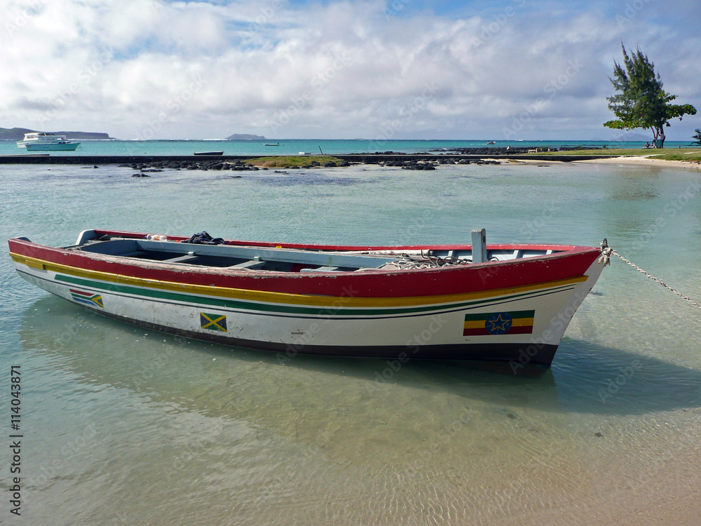 Cap Malheureux, village au nord de l'île Maurice, océan Indien. Un bateau coloré en bois est amarré dans une eau claire et transparente. Au second plan, eau turquoise, ciel bleu et nuages blancs