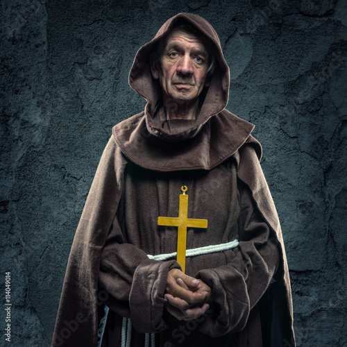 Canvas Print Monk holding a wooden cross in front of the old walls