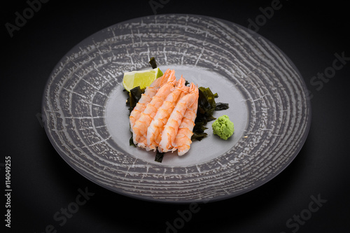 Japanese cuisine. Sushi. Shrimp sashimi on a round plate with lime and wasabi