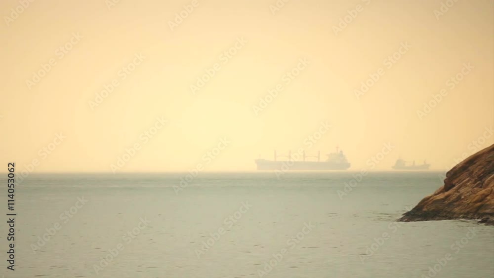 Cargo freighter ship sailing, moving at ocean horizon golden sky in hazy sea Cargo freighter ship sailing, moving at ocean horizon golden sky in hazy sea