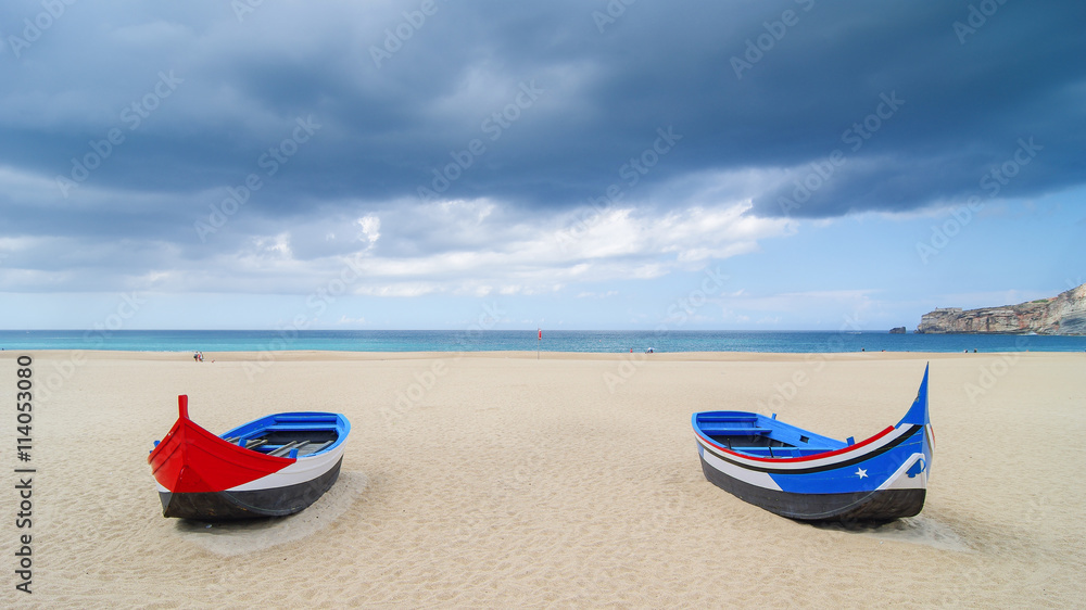 Traditional portuguese boats on the beach of the small touristic city Nazare, Portugal, summer day, after the rain