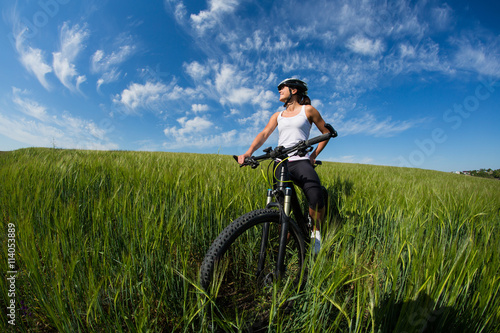 Cheerful beautiful young woman with bike and helmet on field