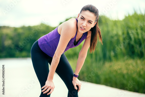 Sport. Recreation before or after workout and running in park. Beautiful woman on purple t-shirt on nature background. Look at one side.