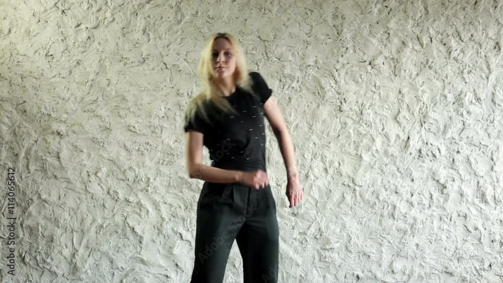 Young hip-hop and house female dancer dressed in black performing against a light wall in the dancing hall Young hip-hop and house female dancer dressed in black performing against a light wall in the dancing hall