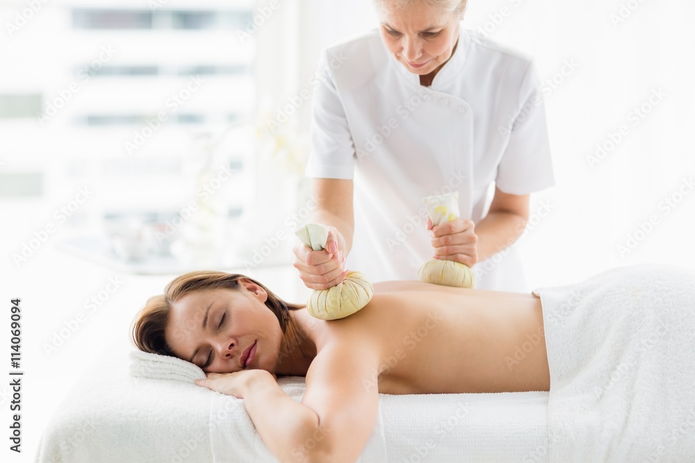 Obraz premium Masseur giving herbal compress massage to woman