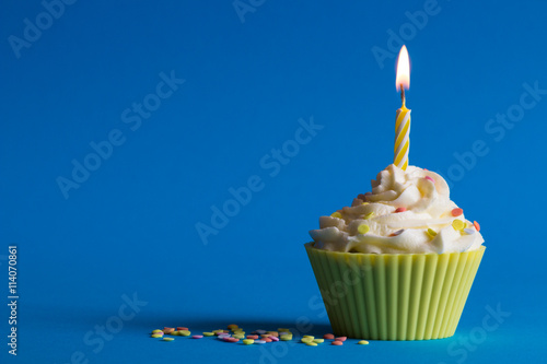 yellow birthday cupcake with burning candle and blue background