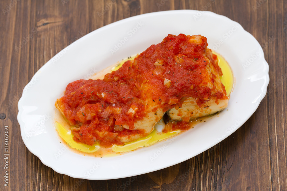 cod fish with tomato sauce on white dish on brown background