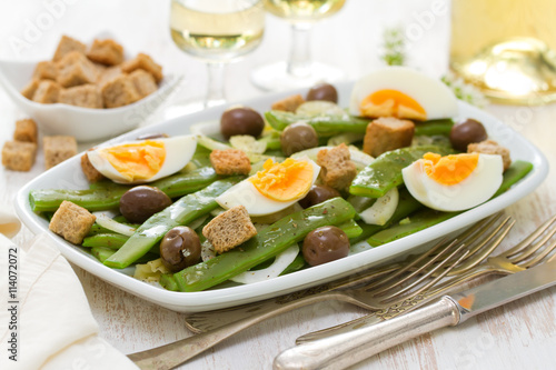 salad green beans with olives and croutins on white dish and glass of white wine