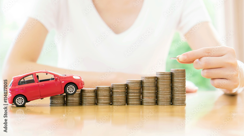 Businesswoman hand pushing a toy car over a stack of coins Businesswoman hand pushing a toy car over a stack of coins