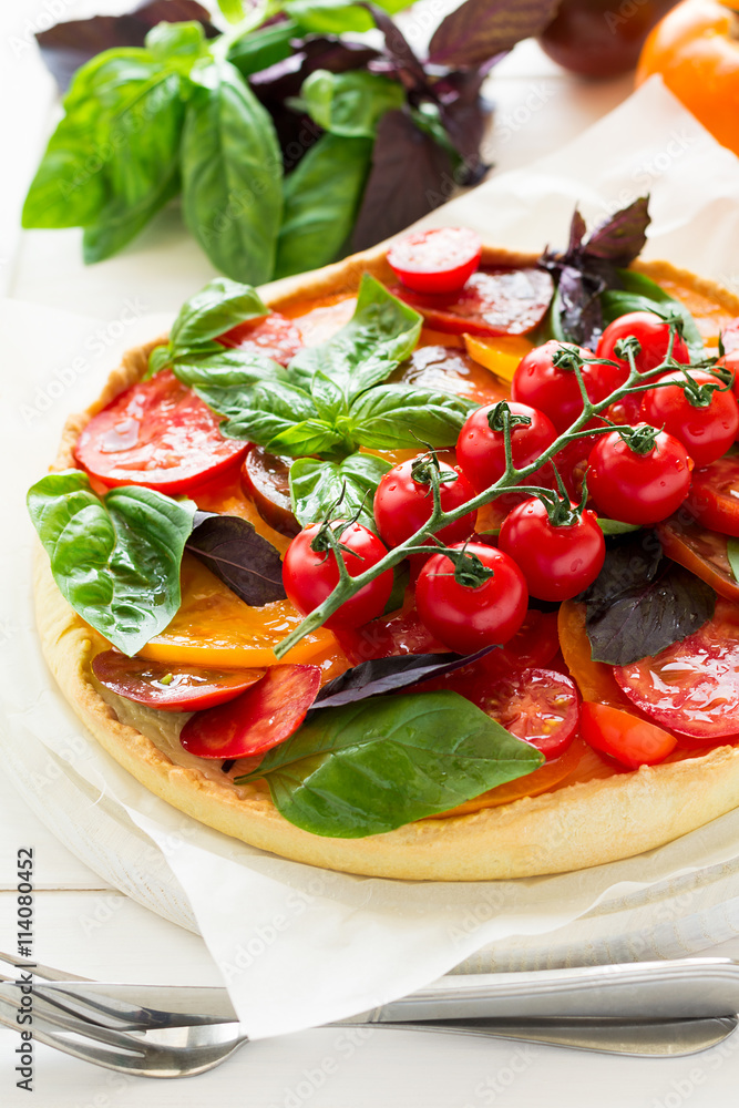 Homemade tart with rikotta, raw tomatoes and basil on white wooden background