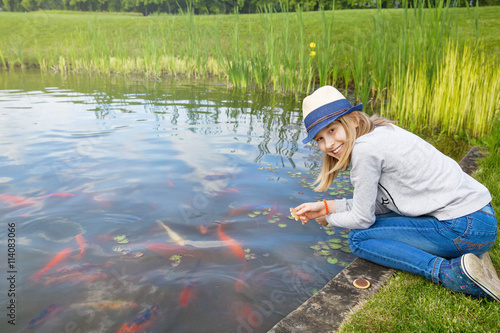 Girl teenager feeding fishes in a pond