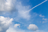 Aircraft contrails among white clouds and blue sky