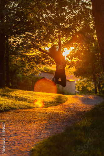 Girl jumps in the sunset till walking on the road.