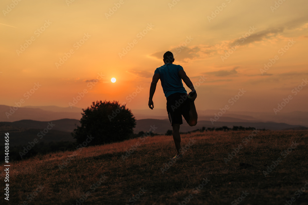 Silhouette of an athletic man in nature in front of a sunset while exercising