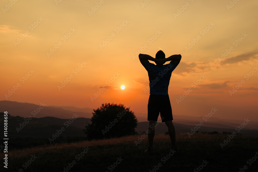 Silhouette of an athletic man in nature in front of a sunset while exercising