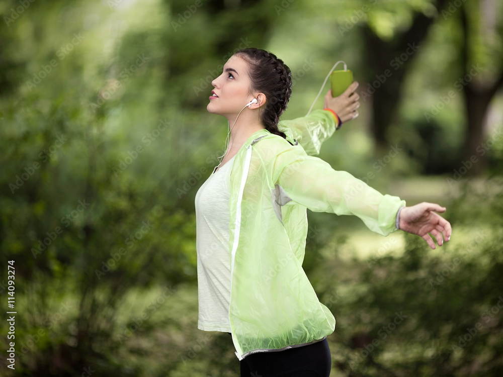 Happy young woman is enjoying music and recreation in nature. She is singing with her and arms outstretched while listening to music on her mobile phone. Happy young woman is enjoying music and recreation in nature. She is singing with her and arms outstretched while listening to music on her mobile phone.