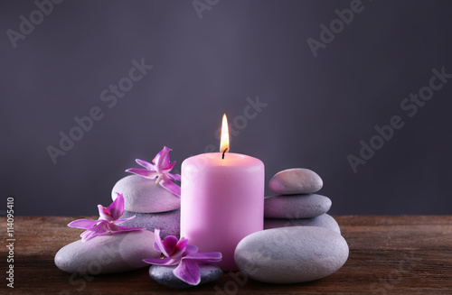 Spa stones with burning candle and flowers on grey background