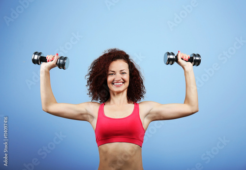 Fotografi Attractive woman exercising with dumb bells on blue background